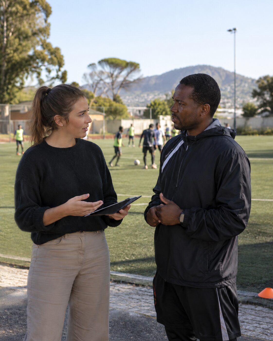 Person discussing sports program activities with a coach beside a soccer field.